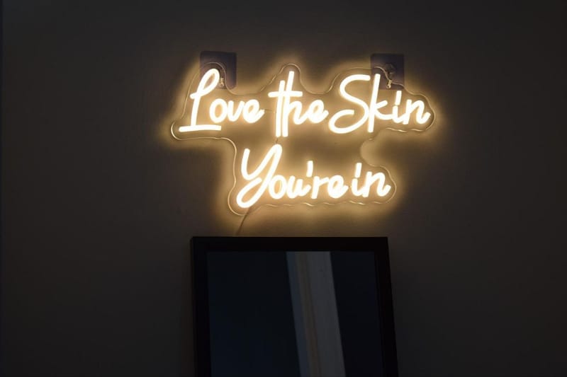 Illuminated Love The Skin You’re In sign on a dark salon wall
